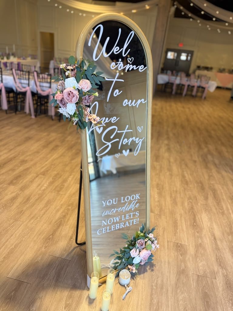 Full-length arched mirror welcome sign with white lettering, dusty rose florals, and pillar candles